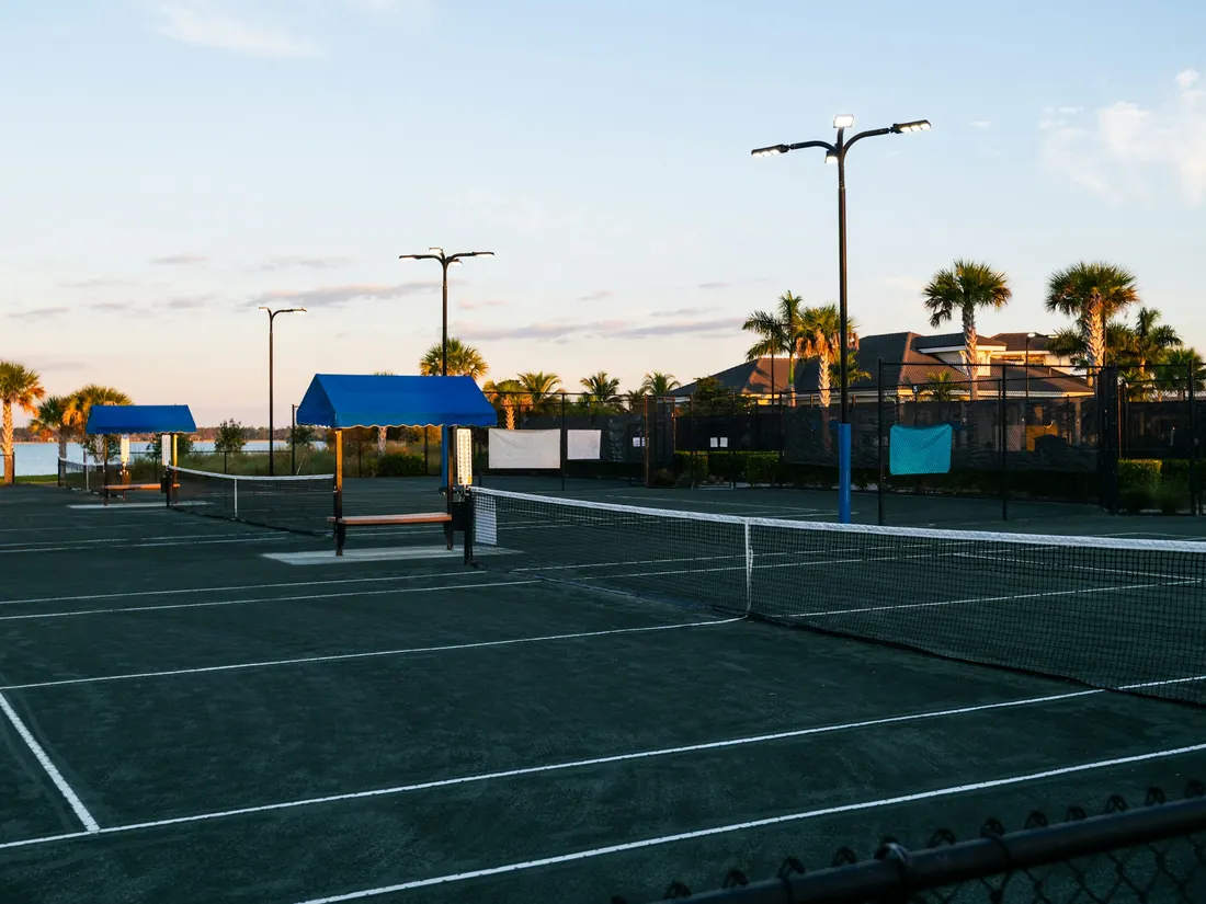 Community tennis courts at sunset with shade canopies and palm trees