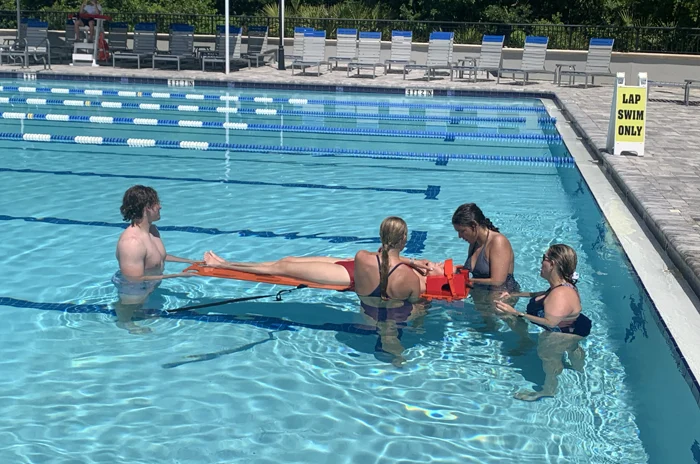 Lifeguard candidates practicing an in-water backboard rescue with a rescue tube
