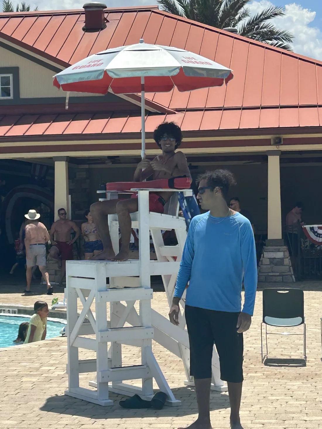Elite lifeguard on an elevated stand under a lifeguard umbrella at a community pool